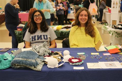 Two students sitting at table with jewelry and crochet crafts.