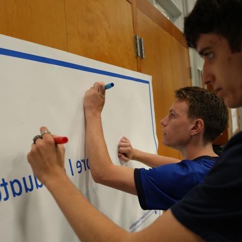 Two students writing on a banner hung on the wall.