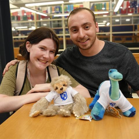 Two students with stuffed dinosaur and stuffed sloth.