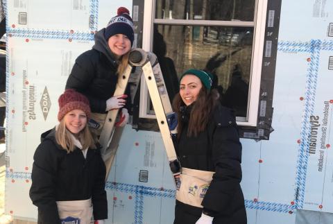 Three women wearing winter clothes standing on/near a ladder while volunteer for Habitat for Humanity