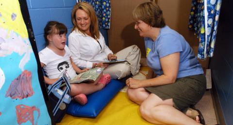 Two adults sit on the floor with a child with Down syndrome