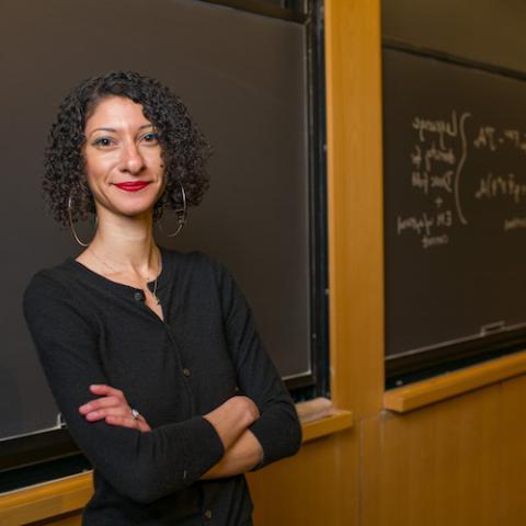 Female professor stands with arms crossed in front of chalkboard