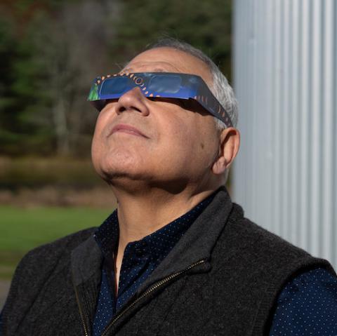 Male space scientist wearing eclipse glasses looks toward the sky