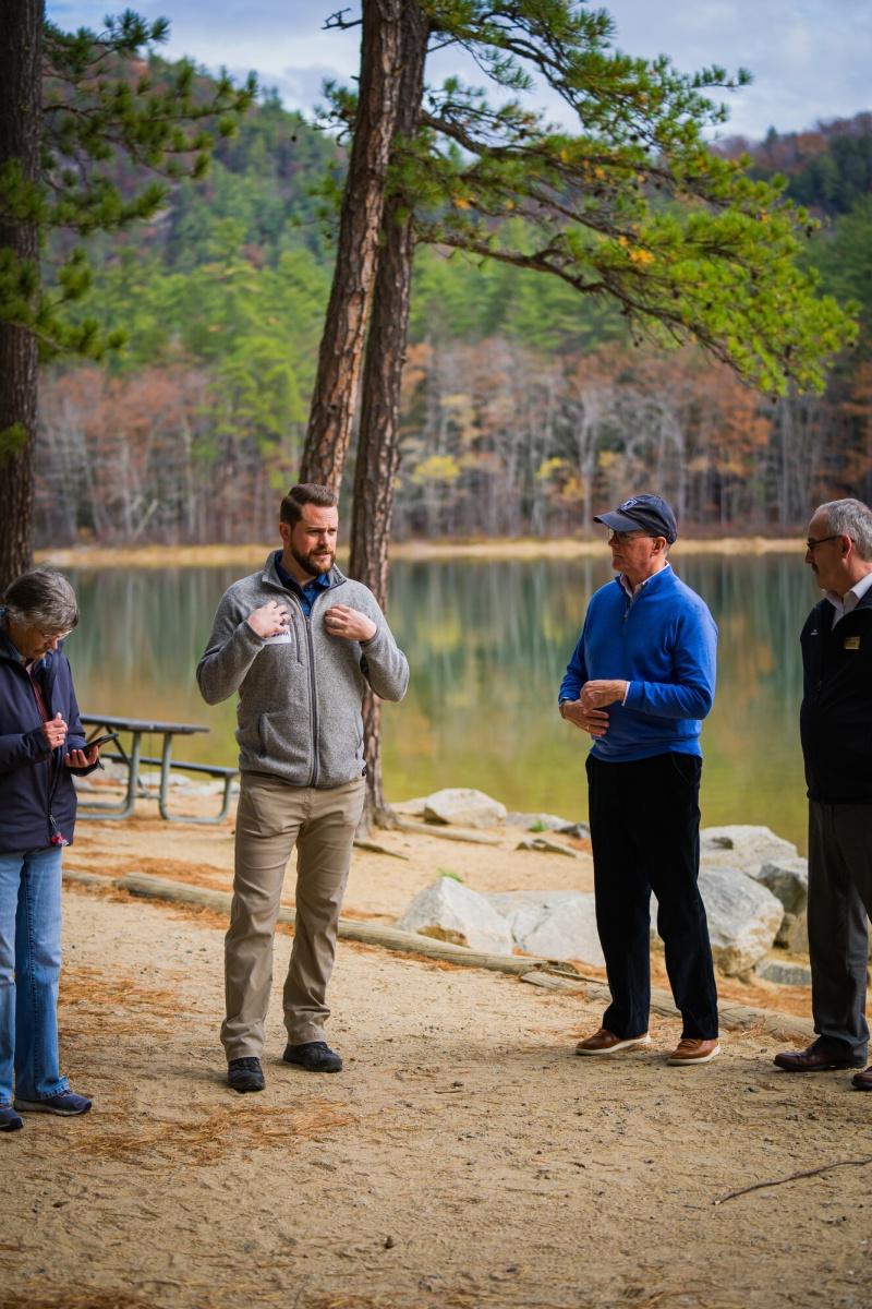 Four people stand talking at the side of a lake.