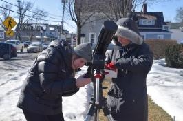 两名女学生穿着保暖的冬装，试图在外面被雪覆盖的人行道上架设望远镜.